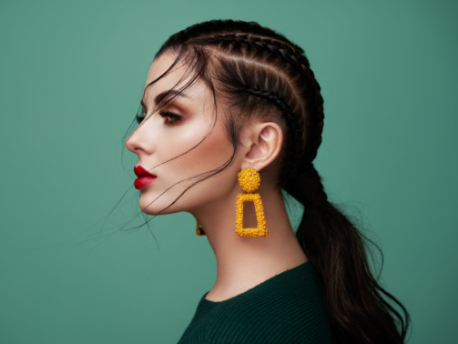 Brunette girl with perfect makeup. Beautiful model woman with curly hairstyle. Care and beauty hair products. Lady with braided hair. Model with jewelry. Turquoise background